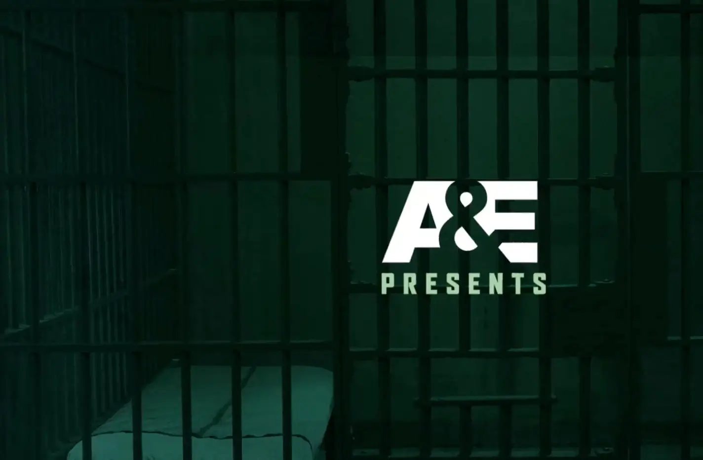 A dimly lit prison cell with a cot, viewed through bars, featuring the logo "a&e presents" in a Sales Content Library.